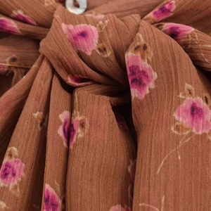 Macro detail of caramel floral chiffon fabric with a white button and tie-knot design