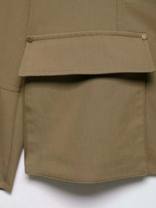 Detail of khaki utility jacket showing twill fabric texture and flap pocket with metal button