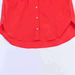 Detail view of red cotton shirt featuring white buttons and a rounded shirttail hemline