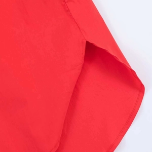 Detail of red loose-fit shirt showing curved hemline and neat side slit stitching