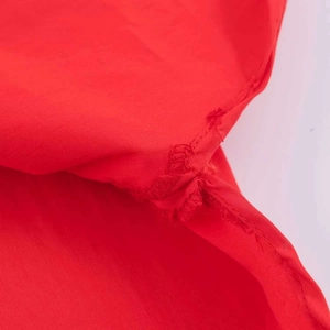 Macro view showing the stitching details and fabric texture of the red loose shirt