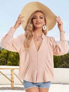 Détail de chemise rose clair à col en V avec boutons décoratifs et manches lanterne