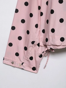 Detail of pink polka dot blouse featuring drawstring hem and pearl-like buttoned cuffs