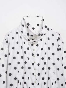 Detailed macro shot of white blouse with black polka dots featuring stand collar and tie