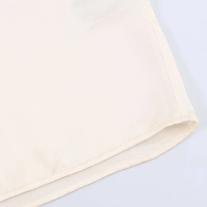 Dettaglio dell'orlo di una camicia di raso bianco crema con cuciture fini e drappeggio liscio