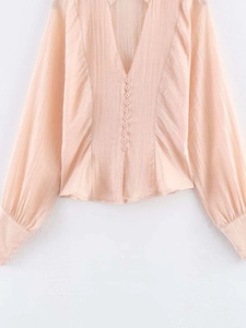 Détail de l'encolure en V profonde avec petits boutons décoratifs sur chemise abricot