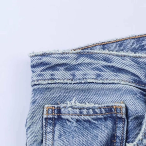 Détail du jean bleu clair avec bords effilochés et coutures contrastées sur la taille
