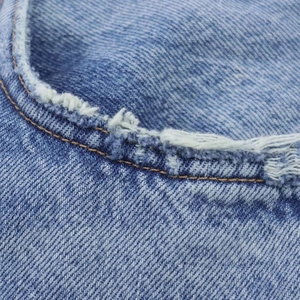Détail du tissu denim bleu clair avec bords effilochés et coutures jaunes contrastées