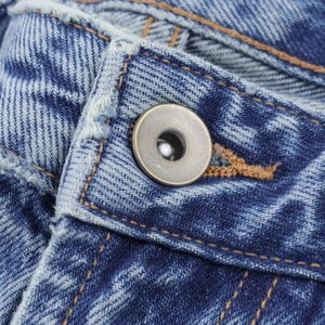 Gros plan du bouton métallique et des coutures sur un jean en denim bleu délavé