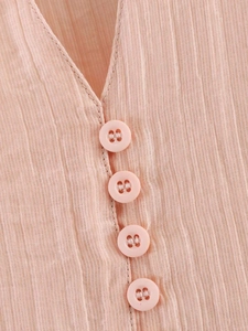Détail de la blouse rose montrant la texture plissée et l'encolure en V boutonnée