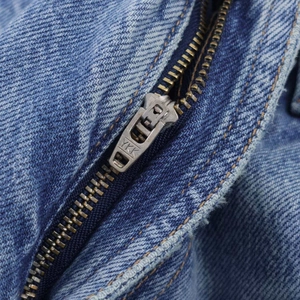 Gros plan détaillé d'une fermeture éclair en métal YKK sur un jean en denim bleu délavé
