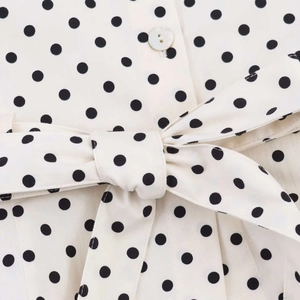 Detail of polka dot fabric with pearlescent button and tied waist belt bow