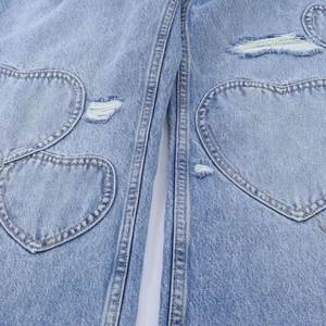 Détail de jean bleu clair avec patchs en forme de cœur et finitions vintage déchirées