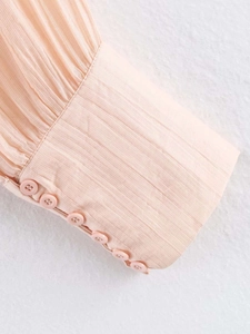 Détail de manche de chemise plissée rose clair avec rangées de boutons assortis