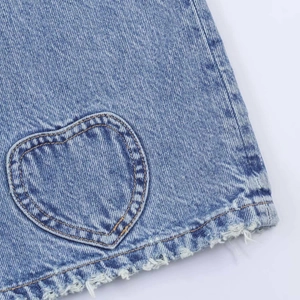 Détail de la poche en forme de cœur et de l'ourlet effiloché sur un jean bleu clair