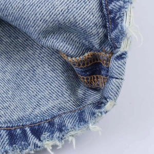 Détail macro du denim délavé bleu clair avec coutures orange et bords effilochés