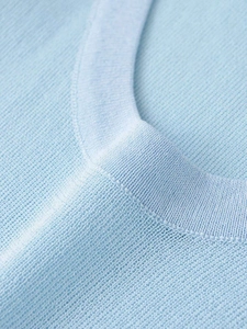 Macro shot of light blue knit top showing fine needlework and round neck seam details