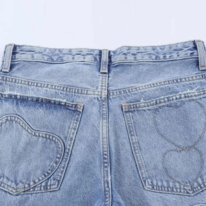 Détail de jean bleu clair montrant la couture de poche en cœur et les bords effilochés