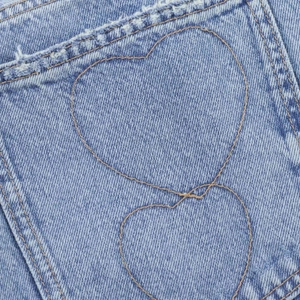 Détail de broderie en forme de cœur sur un jean bleu clair avec bords effilochés