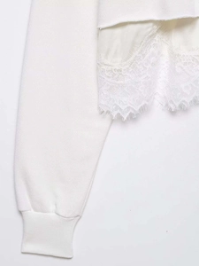 Detailed close-up of white sweatshirt featuring ribbed cuffs and layered lace patchwork trim