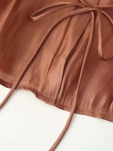 Detail view of caramel pleated satin fabric texture with drawstring tie and wavy hem