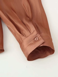 Close-up of rust red satin shirt cuff with silk texture and single button detail