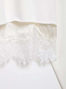 Detail of layered knit hem with satin fabric and delicate eyelash lace trim on white top
