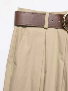 Détail du pantalon large kaki avec une ceinture marron et une grande boucle dorée ronde