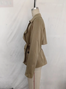 Dettaglio del trench corto kaki con revers classici, spalline e cintura in vita