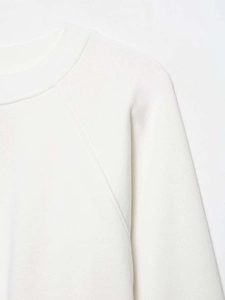 Detail view of the fine knit texture and flat raglan sleeve stitching on white sweatshirt