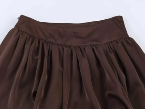 Détail d'une jupe plissée en satin chocolat à taille haute avec texture lisse et soyeuse