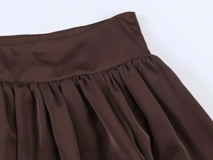Détail d'une jupe en satin à taille haute avec plis et texture de tissu lisse marron foncé