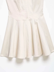 Detailed close-up of the pleated hem and waist stitching on this beige mini dress