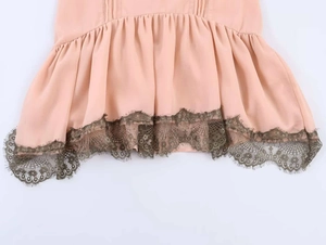 Close-up of light pink dress hem with olive green lace trim and wavy embroidery detail