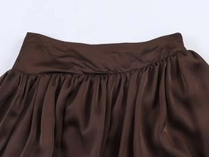 Détail de la jupe midi en satin marron foncé avec taille haute plissée et texture soyeuse