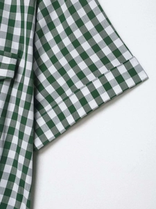 Detailed view of green gingham shirt dress fabric with folded cuff and pocket stitching