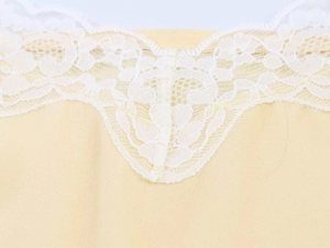 Close-up detail of delicate white floral lace trim on a light yellow camisole neckline