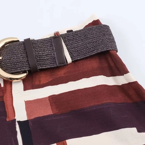 Detail view of abstract geometric print dress featuring a woven brown belt with gold ring buckle