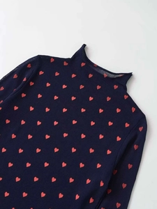 Close-up detail of navy knit sweater with red heart patterns and high mock neck