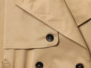 Dettaglio del trench kaki con trama in tessuto twill e chiusura con bottone marrone scuro