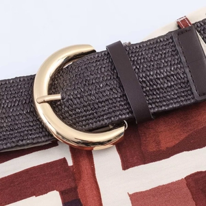 Detail of dark brown braided belt with gold semicircular metal buckle on printed fabric