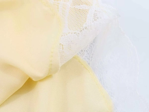 Detailed close-up of light yellow chiffon fabric with delicate white floral lace trim