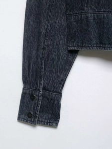 Detailed macro view of dark grey denim jacket with vintage wavy washed texture and cuffs