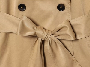 Dettaglio della cintura annodata e bottoni su un trench color kaki in tessuto twill
