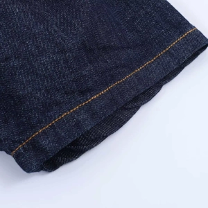 Detailed view of dark indigo denim fabric with contrasting orange stitching and twill texture