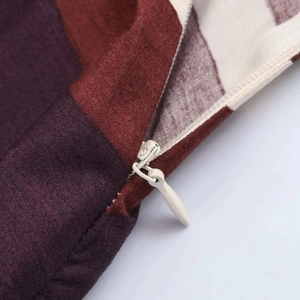 Close-up of invisible zipper detail on red and brown geometric striped cushion cover