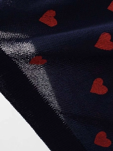 Detail shot of navy blue knit fabric featuring red heart jacquard and fine stitching