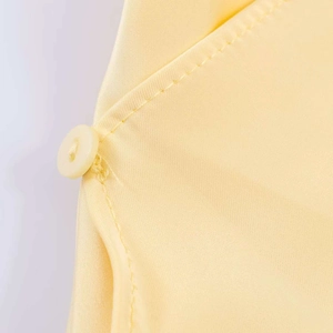 Close-up of pale yellow satin halter top showing detailed stitching and matching button