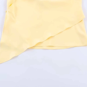 Detail of light yellow satin halter top showing asymmetric overlapping hem design