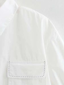 Nahaufnahme eines weißen Kurzarmhemdes mit schwarzen Kontrastnähten an der Vordertasche
